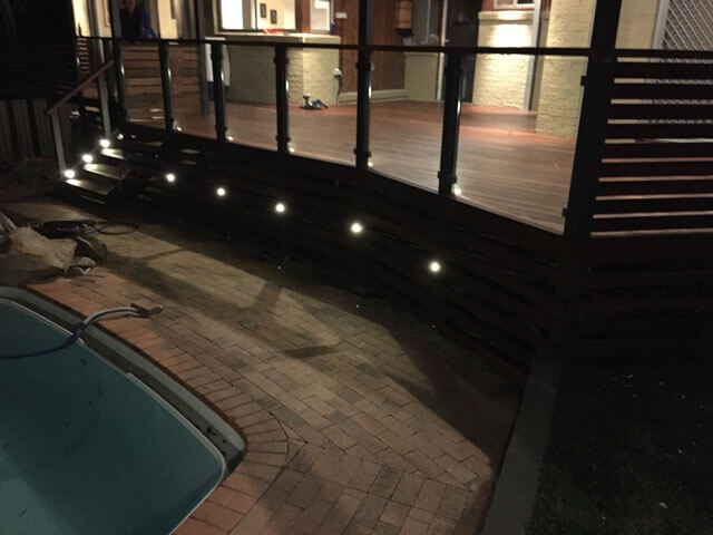 Deck lights installed into wood and illuminating pool